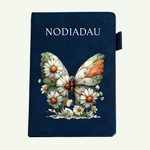 A dark navy blue notebook or journal with the word 'NODIADAU' printed in white at the top, decorated with a large butterfly and daisy illustration on the front cover.
