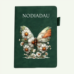 A dark green notebook or journal with the word 'NODIADAU' printed at the top and an illustrated butterfly surrounded by white daisies on the front cover, shown against a light off-white background.