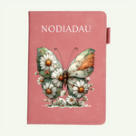 A pink notebook with a butterfly and daisy illustration on the cover, shown against a light off-white background.