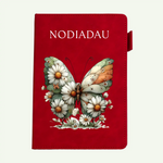 A red notebook or journal cover featuring the word 'NODIADAU' in white at the top and an illustrated butterfly made of daisy-like flowers in the center, shown on a plain light background.