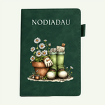 A dark green journal or notebook with the word 'NODIADAU' printed at the top and an illustration of gardening boots, a flower pot, daisies, and a hand on the front cover, shown against a light off-white background.